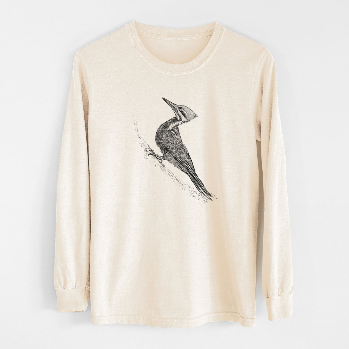 Ivory Comfort Colors long sleeve shirt laid flat, printed with a black ink illustration of a pileated woodpecker clinging to a tree trunk.
