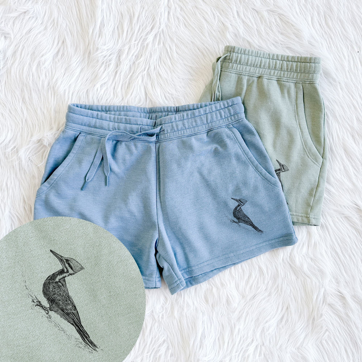 Two pairs of Cali Wave shorts in different colors printed with a black ink illustration of a pileated woodpecker clinging to a tree trunk, with a close-up of the print.