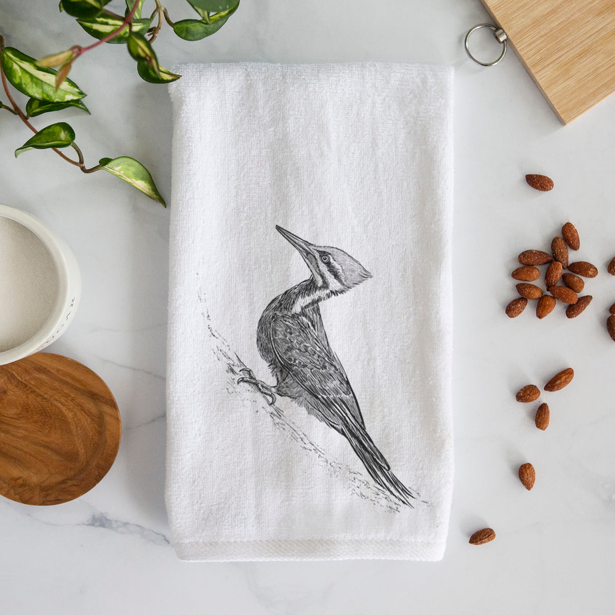 White hand towel printed with a black ink illustration of a pileated woodpecker clinging to a tree trunk.