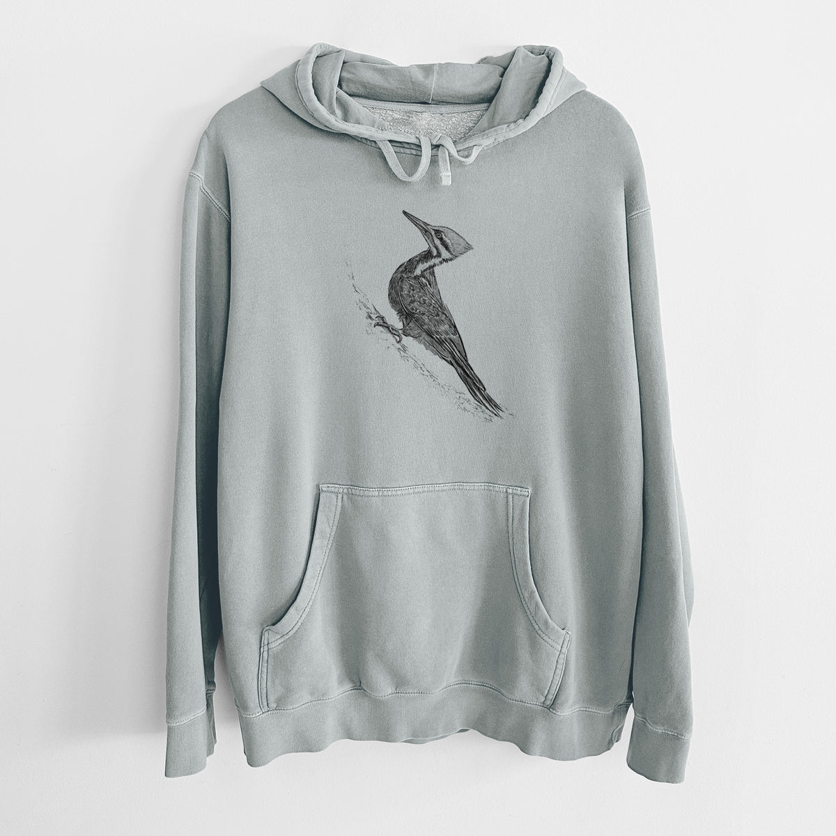 Sage green pigment dyed hoodie laid flat, printed with a black ink illustration of a pileated woodpecker clinging to a tree trunk.