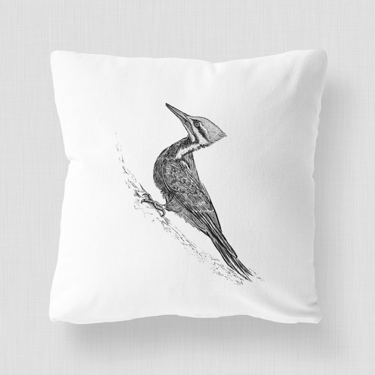 White pillow cover printed with a black ink illustration of a pileated woodpecker clinging to a tree trunk.