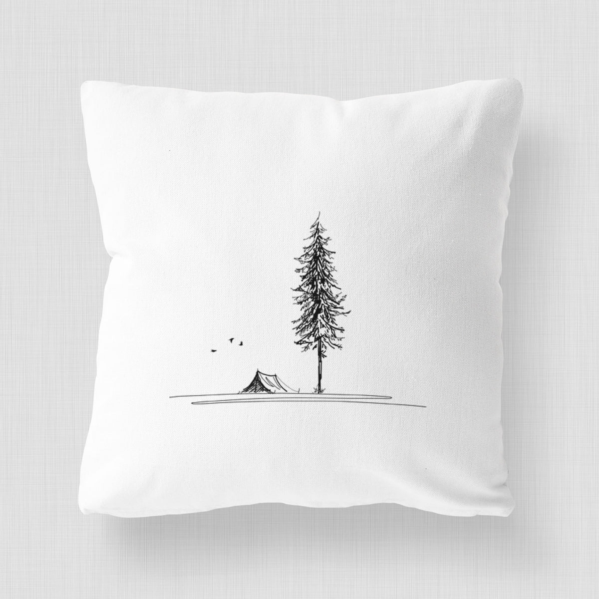 White pillow cover printed with a black ink illustration of a tall pine tree beside a small tent on a hill.