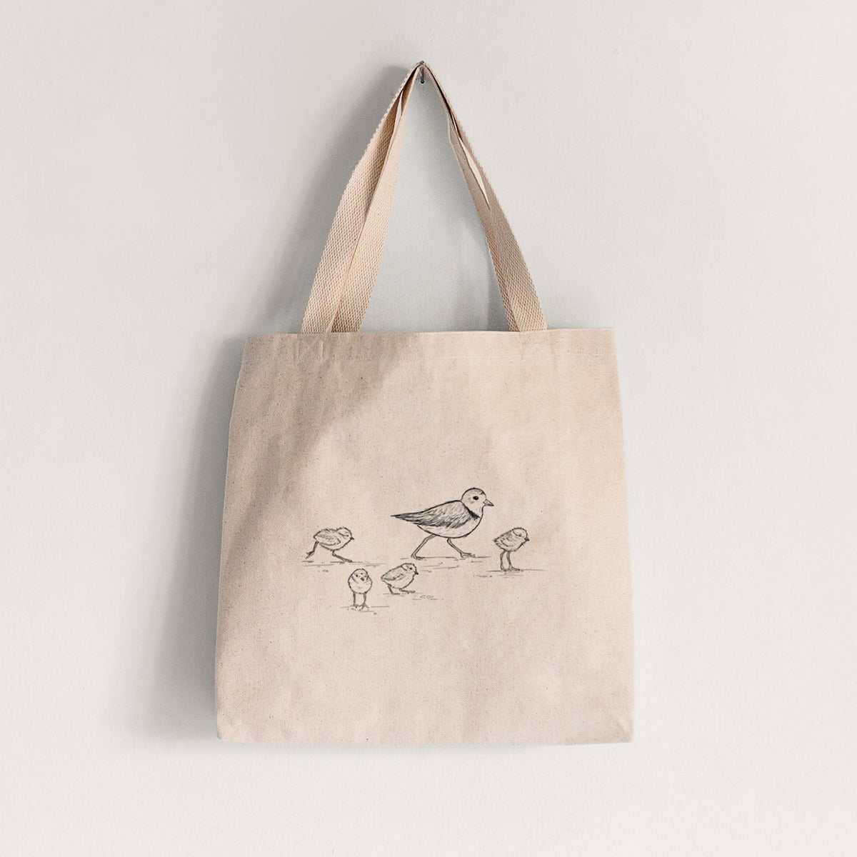Natural canvas tote bag printed with a black ink sketch of a piping plover with its chicks on the sand.