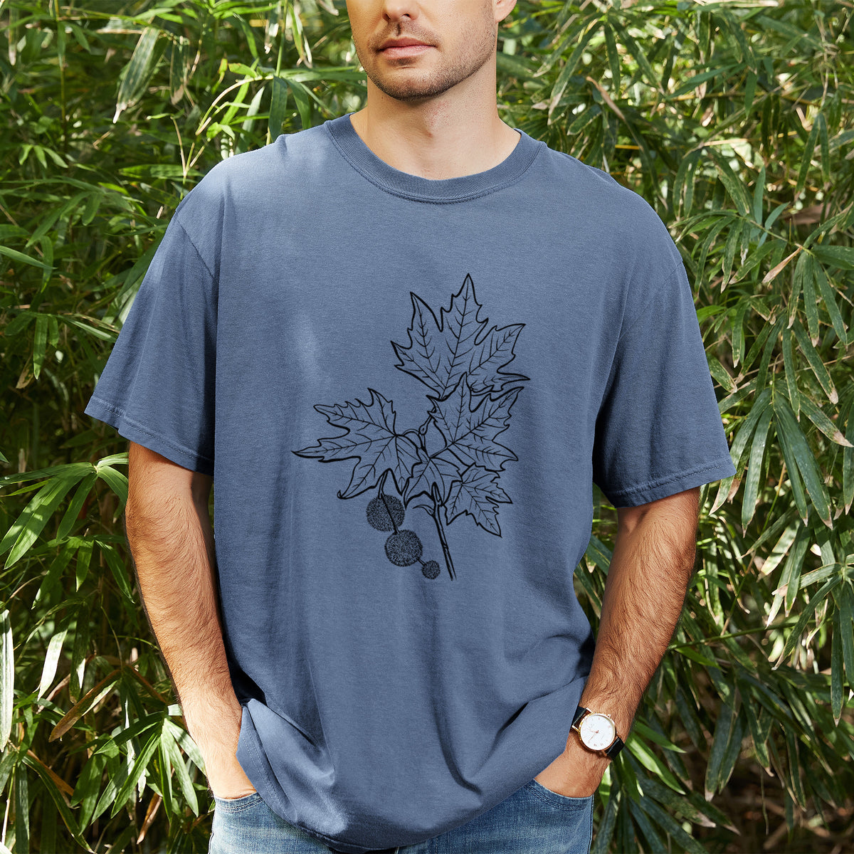 Man wearing a Comfort Colors t-shirt printed with a black ink illustration of an oriental plane tree branch with lobed leaves and round seed balls, outdoors.
