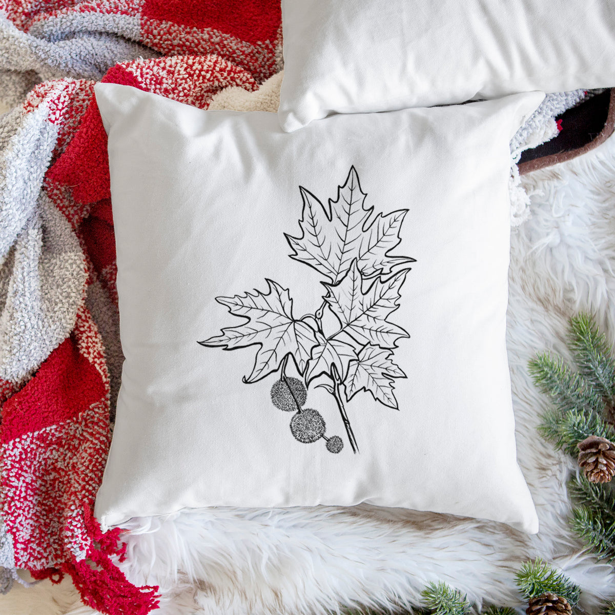 White pillow cover printed with a black ink illustration of an oriental plane tree branch with lobed leaves and round seed balls, on a woven chair.
