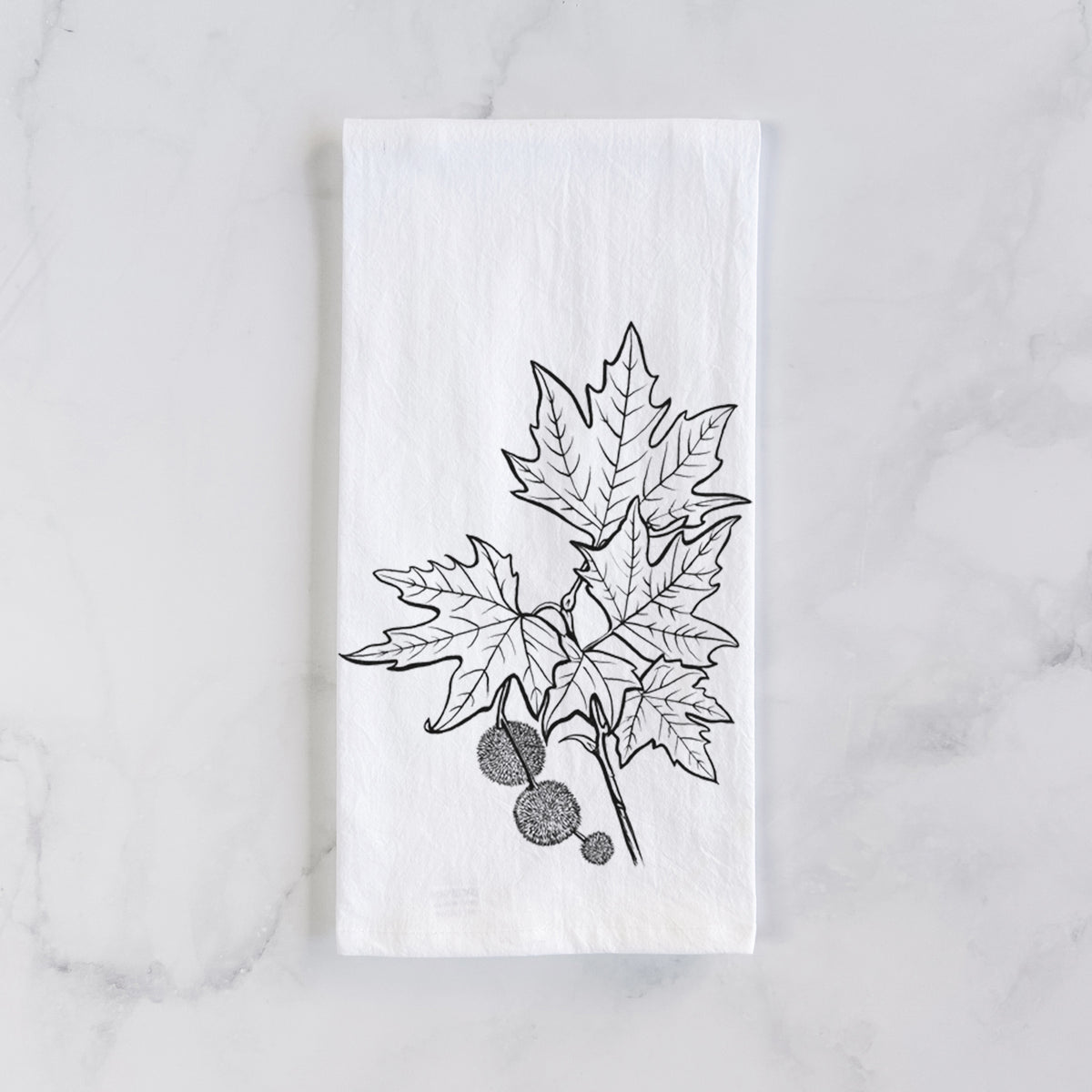 White cotton tea towel laid flat on marble, printed with a black ink illustration of an oriental plane tree branch with lobed leaves and round seed balls.