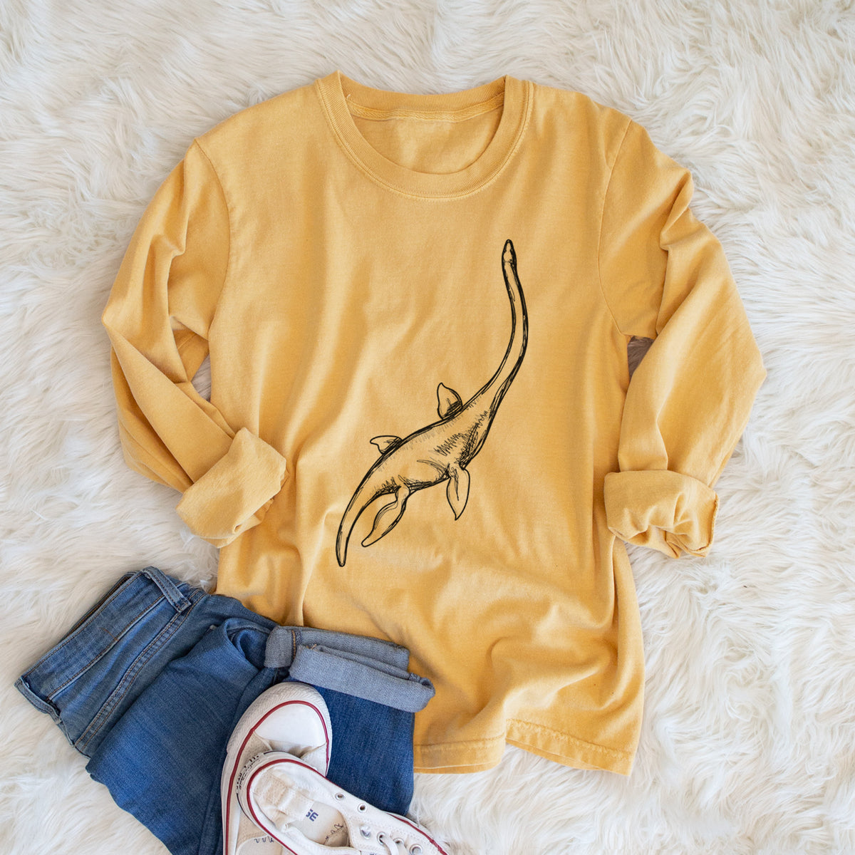 Golden wheat yellow Comfort Colors long sleeve shirt printed with a black ink illustration of a long-necked plesiosaur swimming, shown in a lifestyle photo.