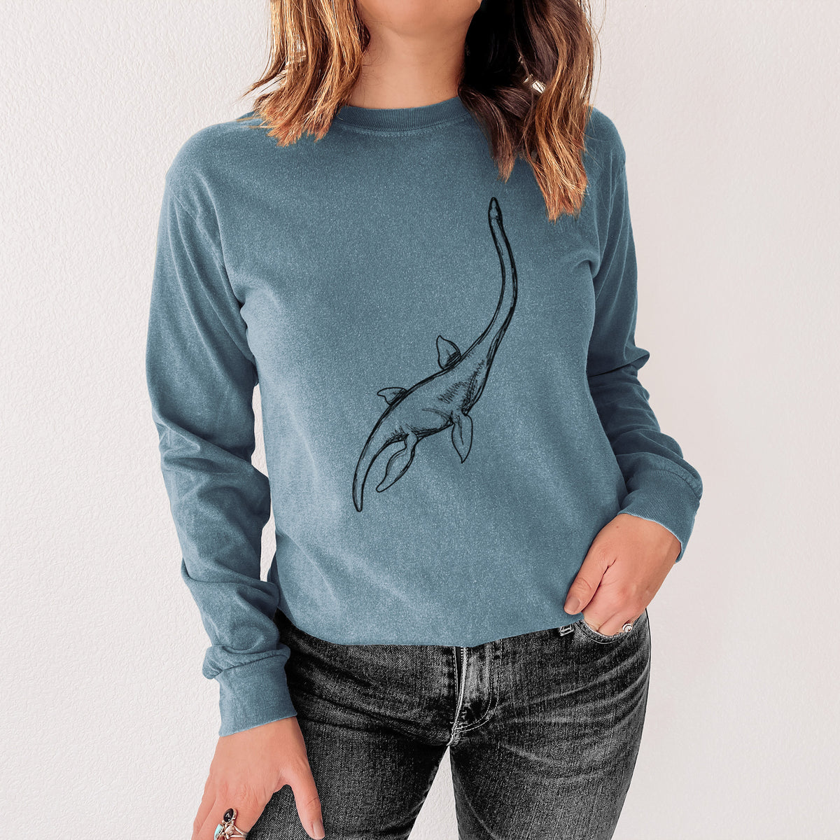 Steel blue Comfort Colors long sleeve shirt printed with a black ink illustration of a long-necked plesiosaur swimming, shown in a lifestyle photo.