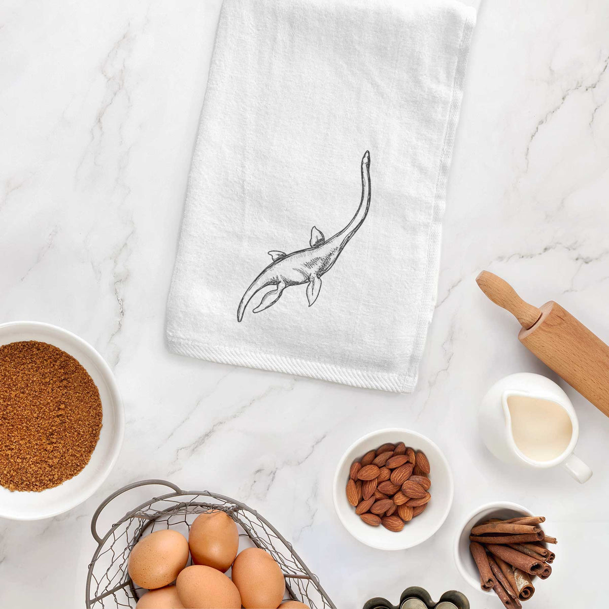 White hand towel printed with a black ink illustration of a long-necked plesiosaur swimming, hanging on a cabinet door.