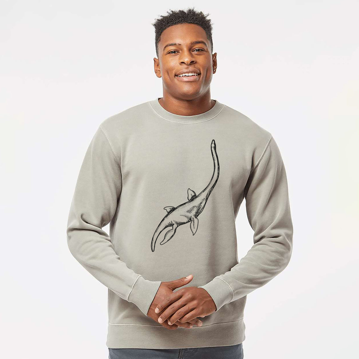 Model wearing a cement grey pigment dyed crewneck sweatshirt printed with a black ink illustration of a long-necked plesiosaur swimming.