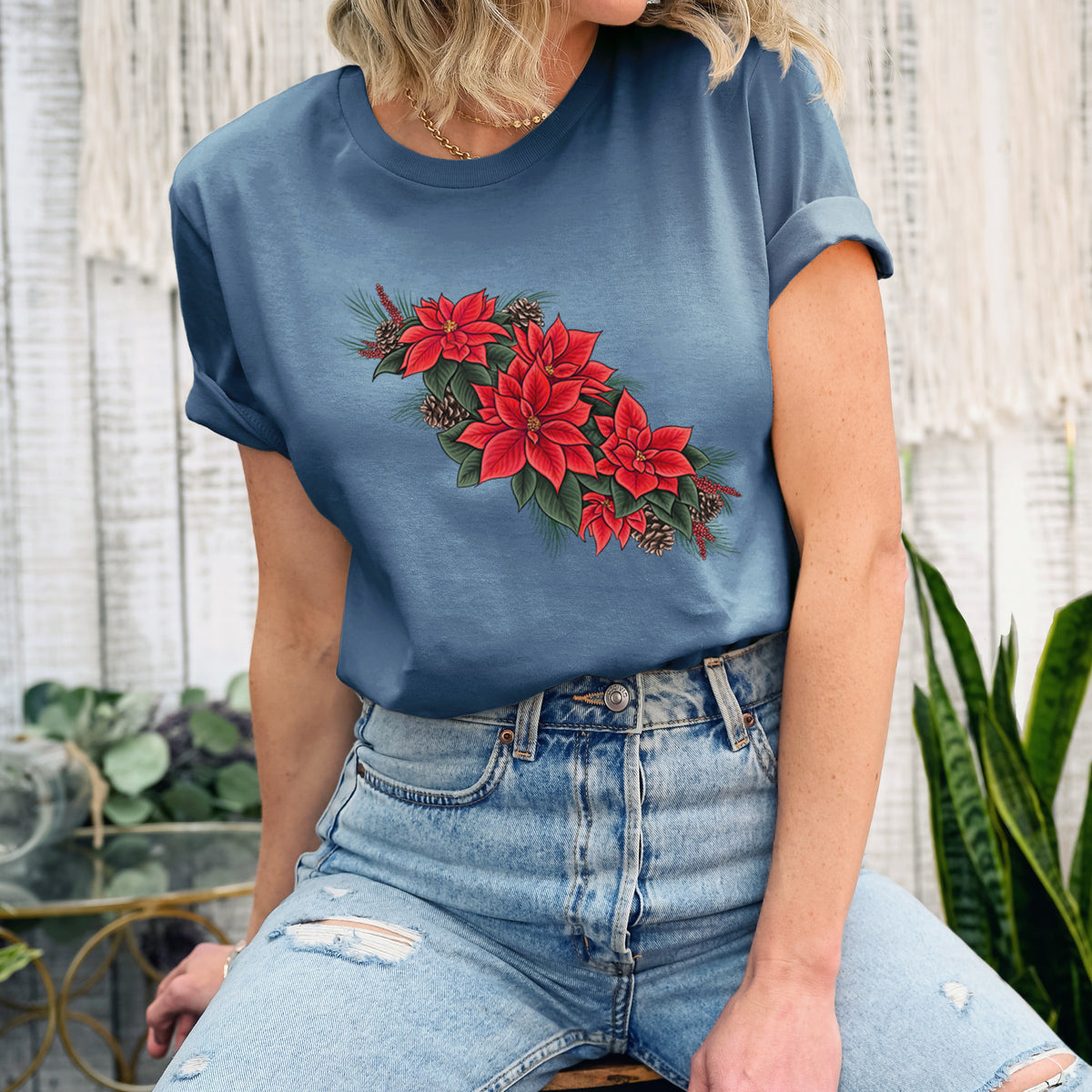 Woman wearing a steel blue lightweight cotton t-shirt printed with a full-color illustration of red poinsettia flowers with pine greenery and pine cones.