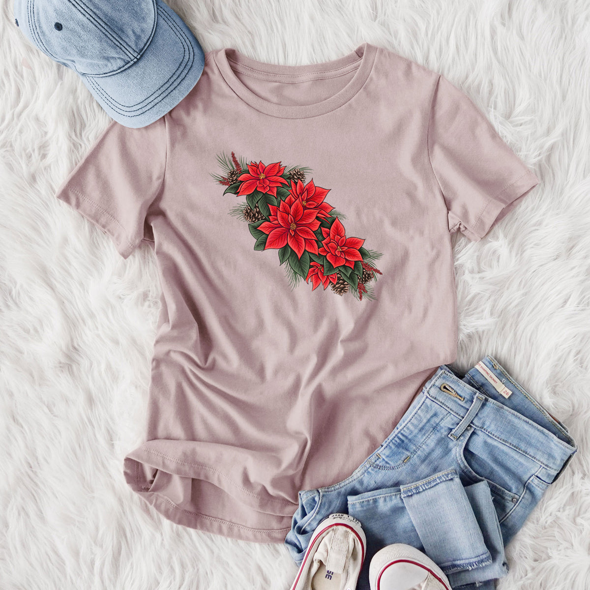 Women's relaxed fit cotton t-shirt printed with a full-color illustration of red poinsettia flowers with pine greenery and pine cones, styled flat on a white faux fur rug with jeans.