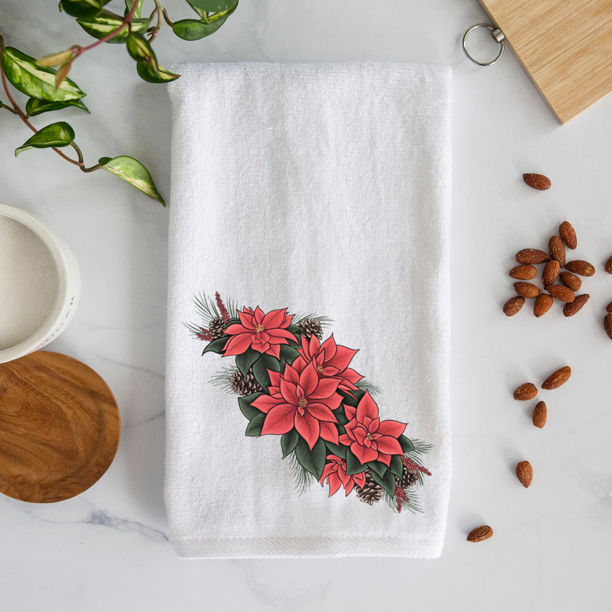 White hand towel printed with a full-color illustration of red poinsettia flowers with pine greenery and pine cones.
