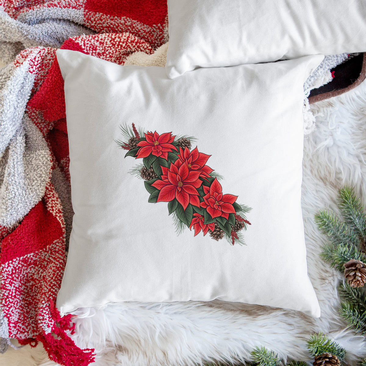 White pillow cover printed with a full-color illustration of red poinsettia flowers with pine greenery and pine cones, on a woven chair.