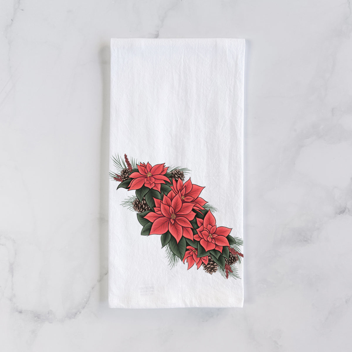 White cotton tea towel laid flat on marble, printed with a full-color illustration of red poinsettia flowers with pine greenery and pine cones.