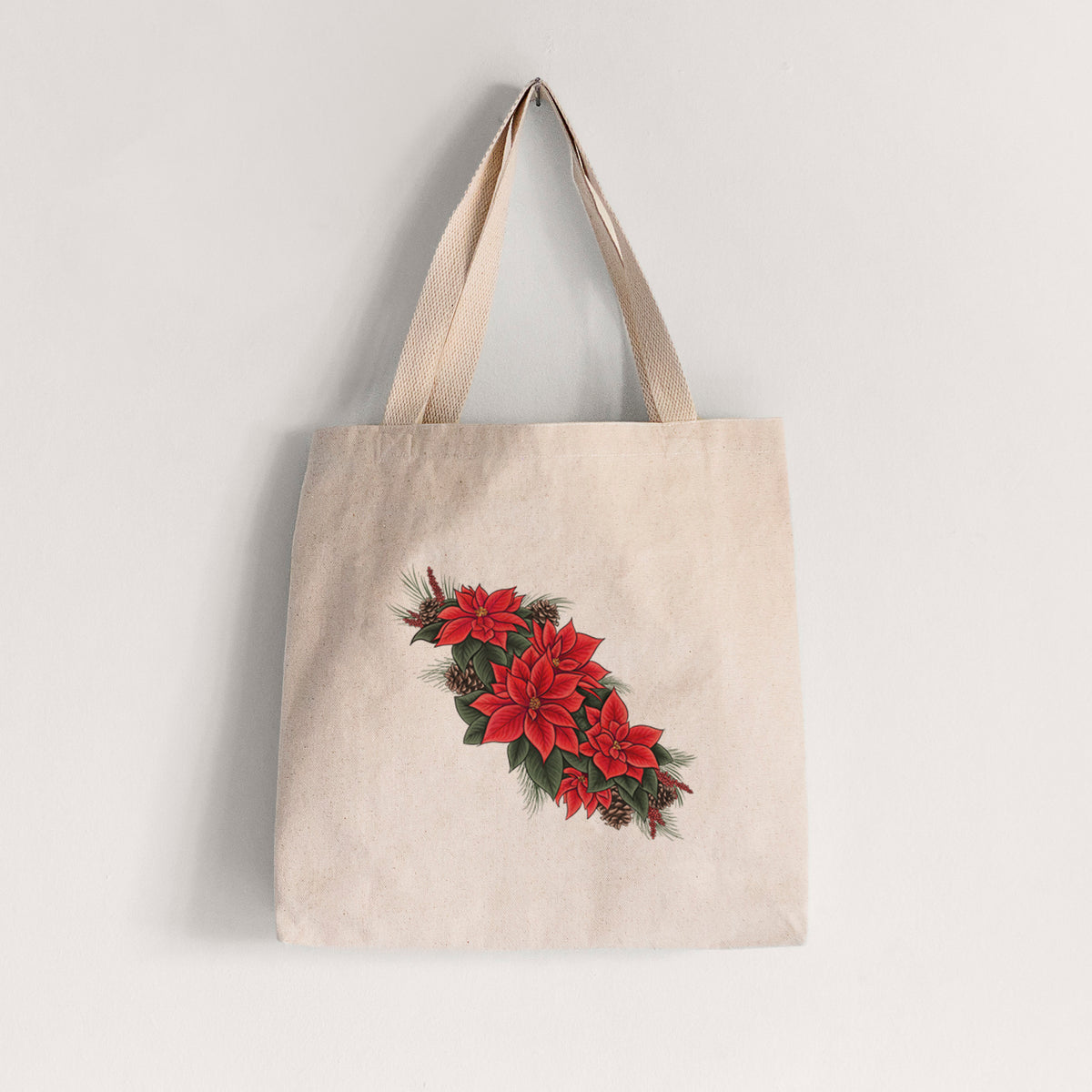 Natural canvas tote bag printed with a full-color illustration of red poinsettia flowers with pine greenery and pine cones.