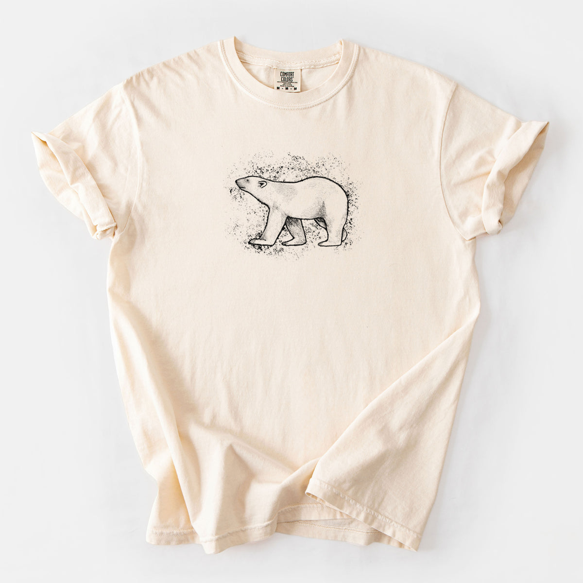 Ivory Comfort Colors t-shirt laid flat, printed with a black ink illustration of a polar bear walking across snow.