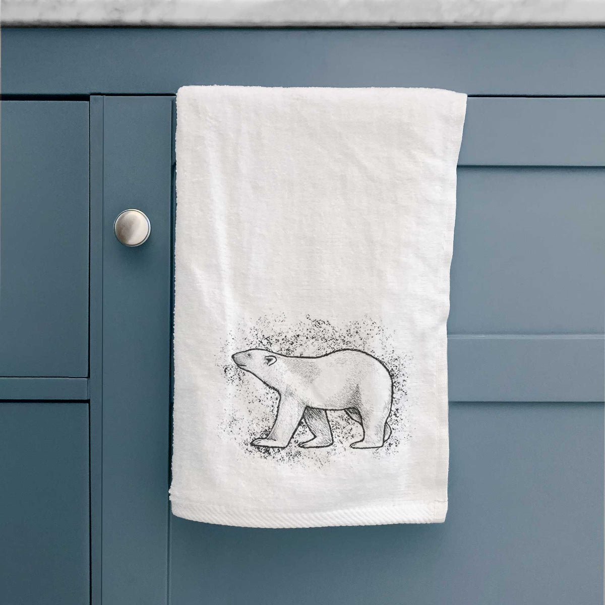 White hand towel printed with a black ink illustration of a polar bear walking across snow, hanging on a cabinet door.