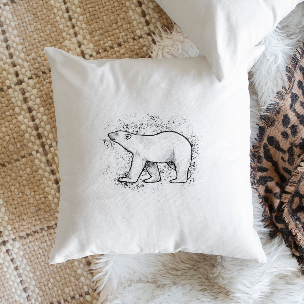 White pillow cover printed with a black ink illustration of a polar bear walking across snow, on a woven chair.