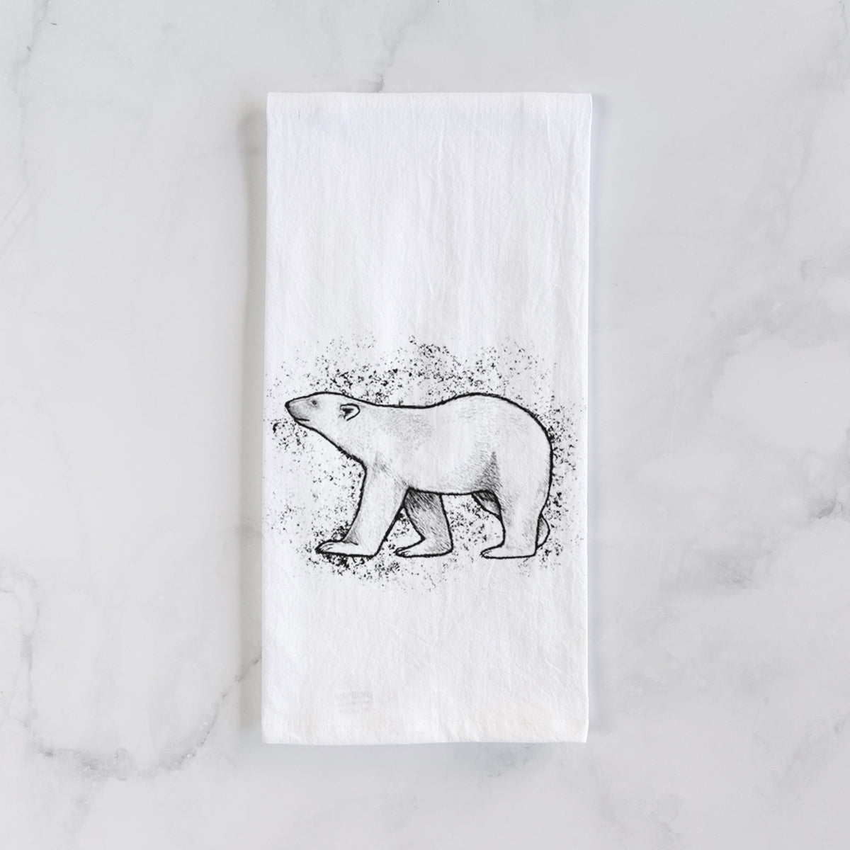 White cotton tea towel laid flat on marble, printed with a black ink illustration of a polar bear walking across snow.