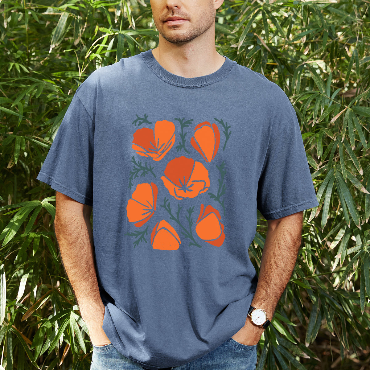 Man wearing a Comfort Colors t-shirt printed with a full-color illustration of orange California poppies with blue-green leaves, outdoors.