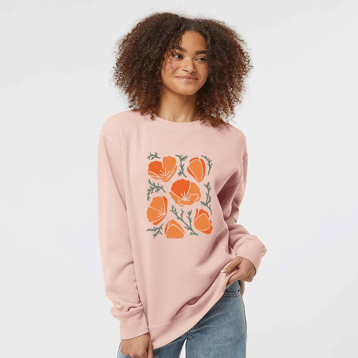 Model wearing a dusty pink pigment dyed crewneck sweatshirt printed with a full-color illustration of orange California poppies with blue-green leaves.