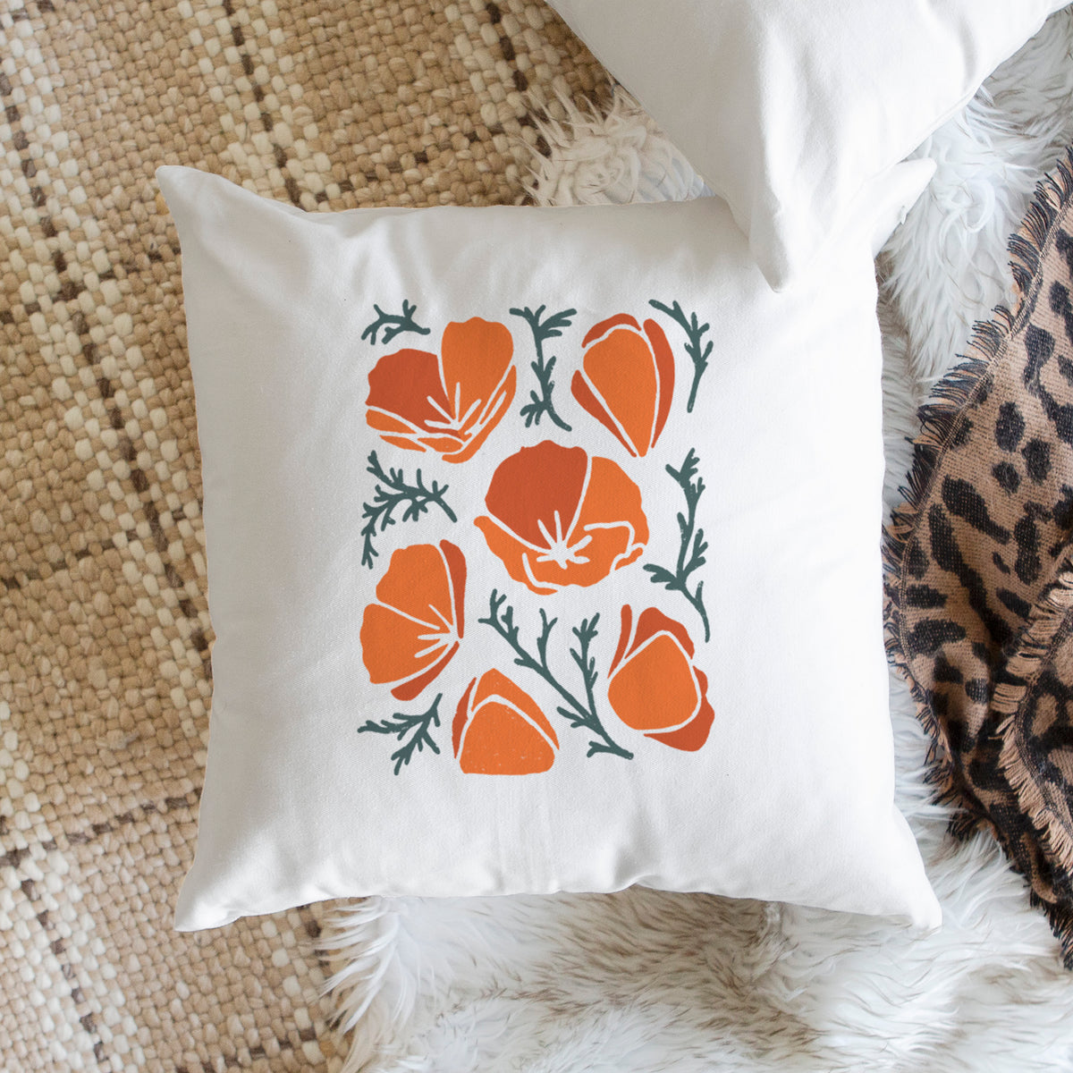 White pillow cover printed with a full-color illustration of orange California poppies with blue-green leaves, on a woven chair.