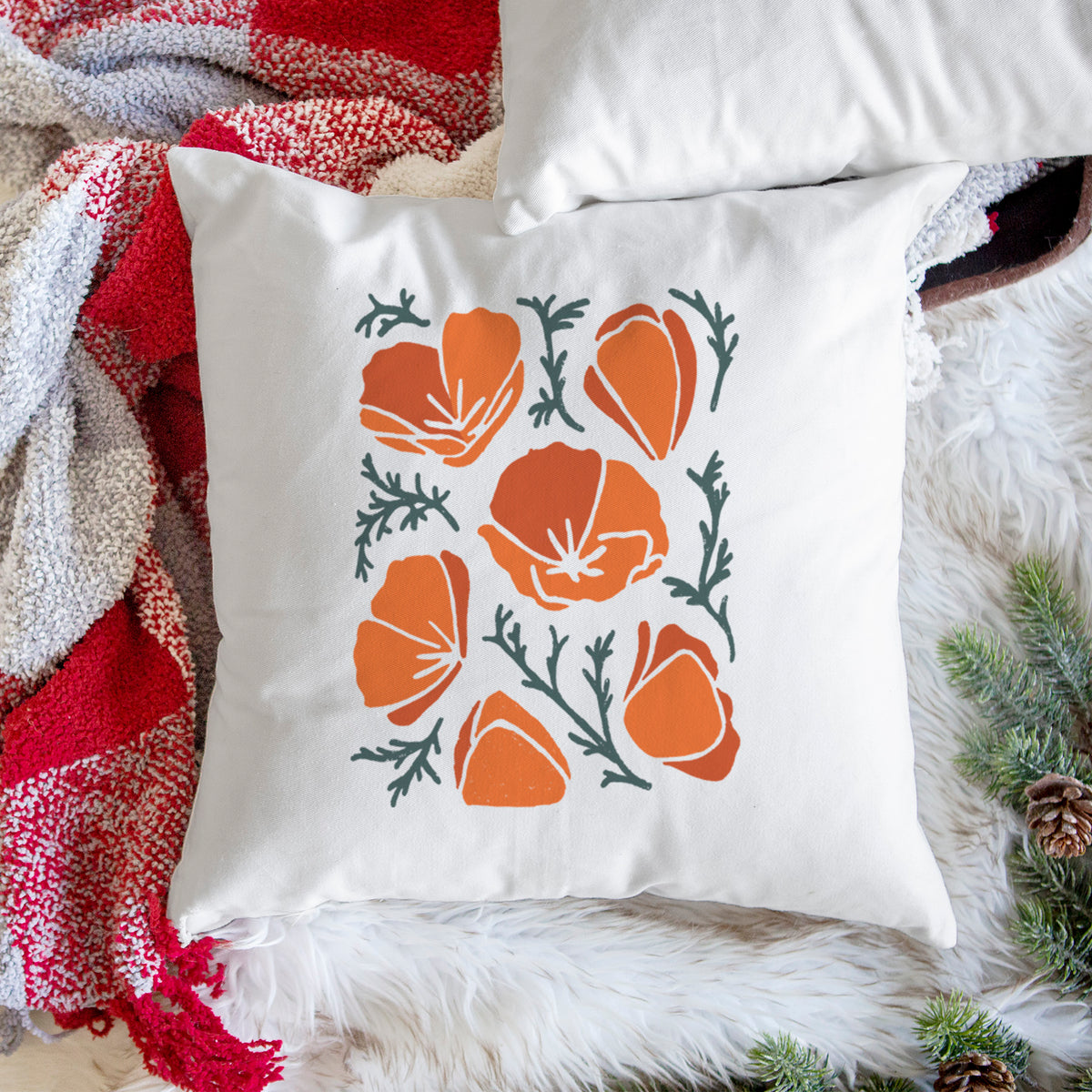 White pillow cover printed with a full-color illustration of orange California poppies with blue-green leaves, on a woven chair.