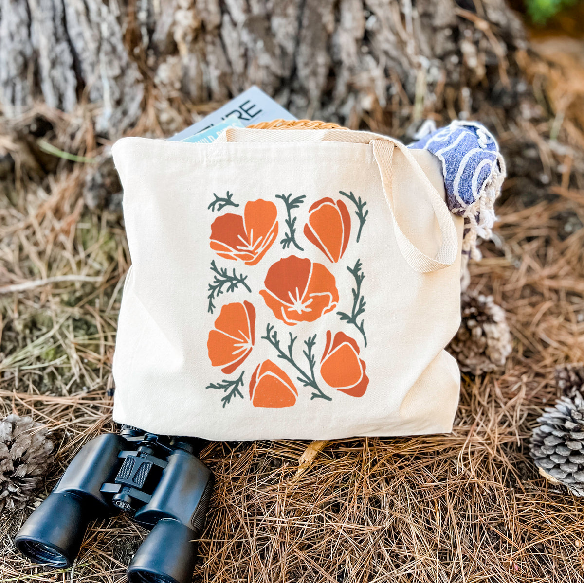 Canvas tote bag printed with a full-color illustration of orange California poppies with blue-green leaves, resting on dry grass beside a pair of binoculars.