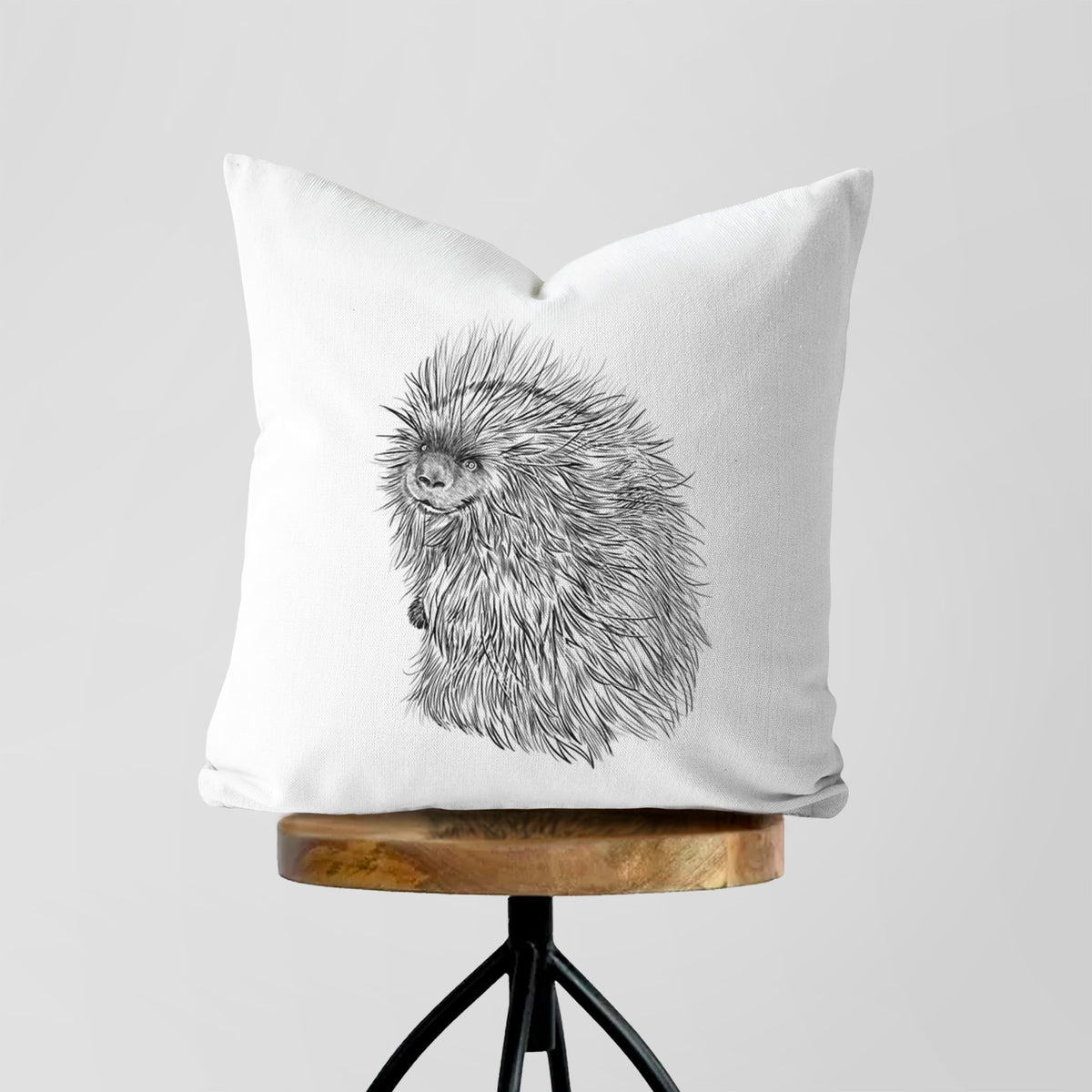 White pillow cover printed with a detailed black ink illustration of a porcupine with its quills raised, on a wooden stool.