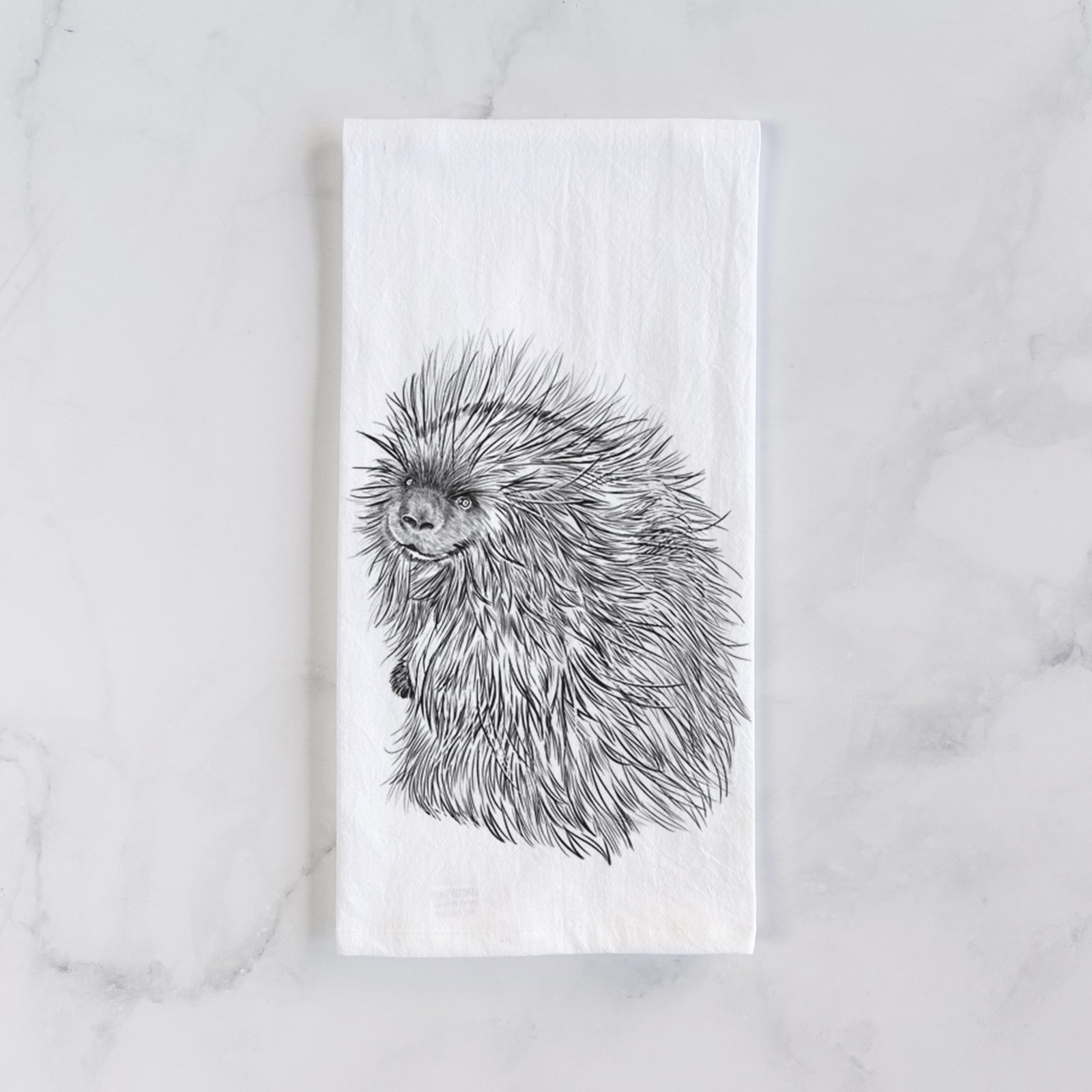 White cotton tea towel printed with a detailed black ink illustration of a porcupine with its quills raised, on a marble counter beside a round wooden cutting board and greenery.