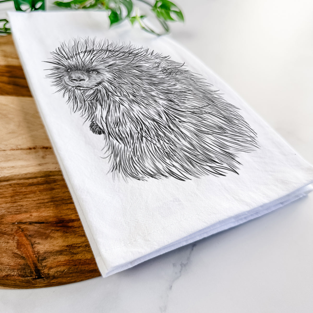 Close-up of a folded white tea towel on a wooden board, showing a detailed black ink illustration of a porcupine with its quills raised.
