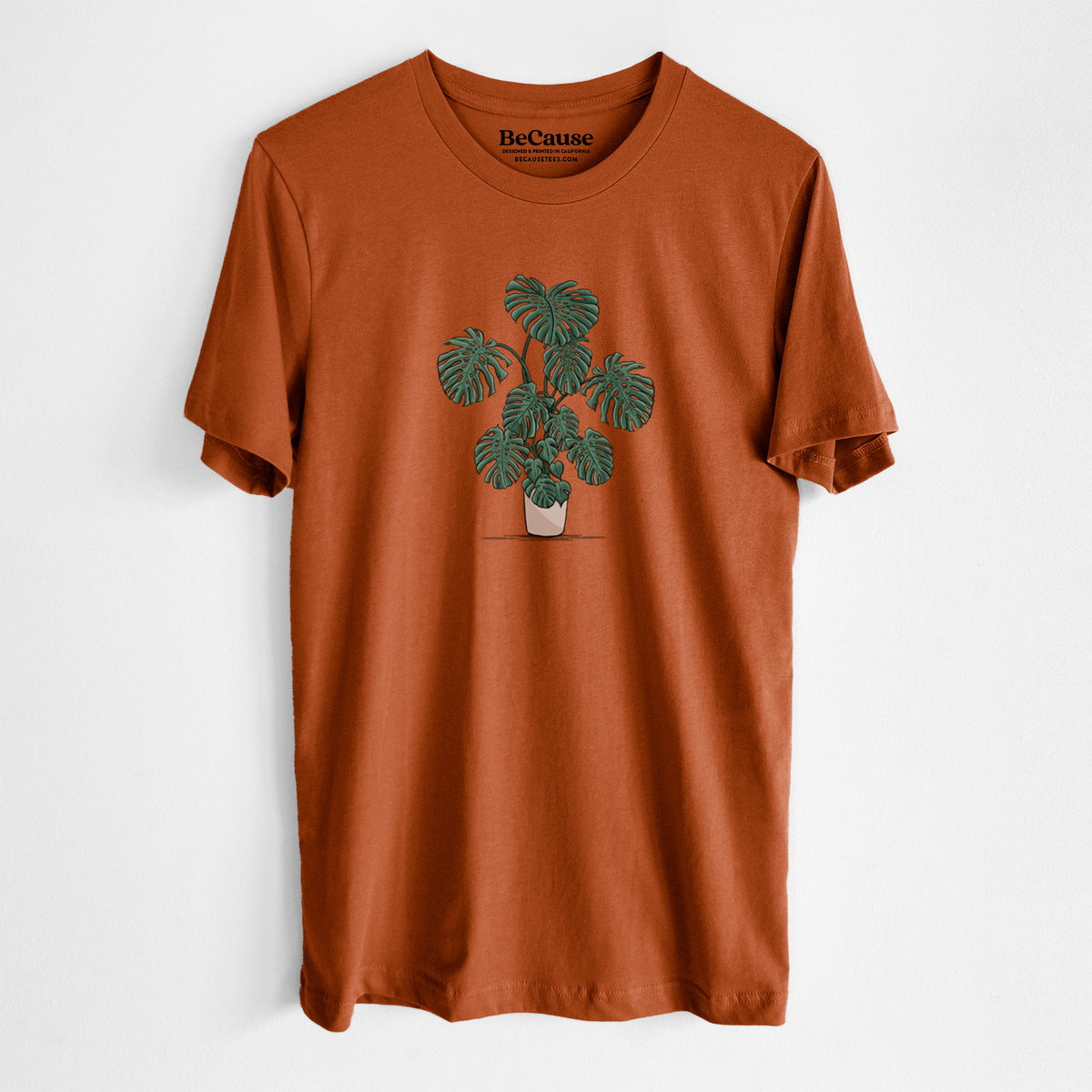 Autumn lightweight cotton t-shirt laid flat, printed with a full-color illustration of a large potted Monstera plant.