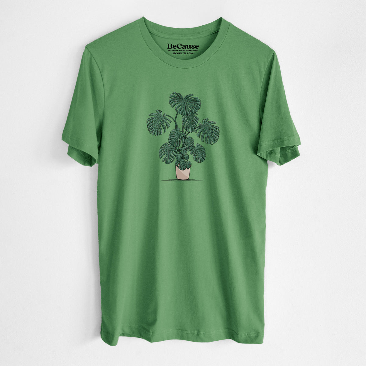 Leaf green lightweight cotton t-shirt laid flat, printed with a full-color illustration of a large potted Monstera plant.