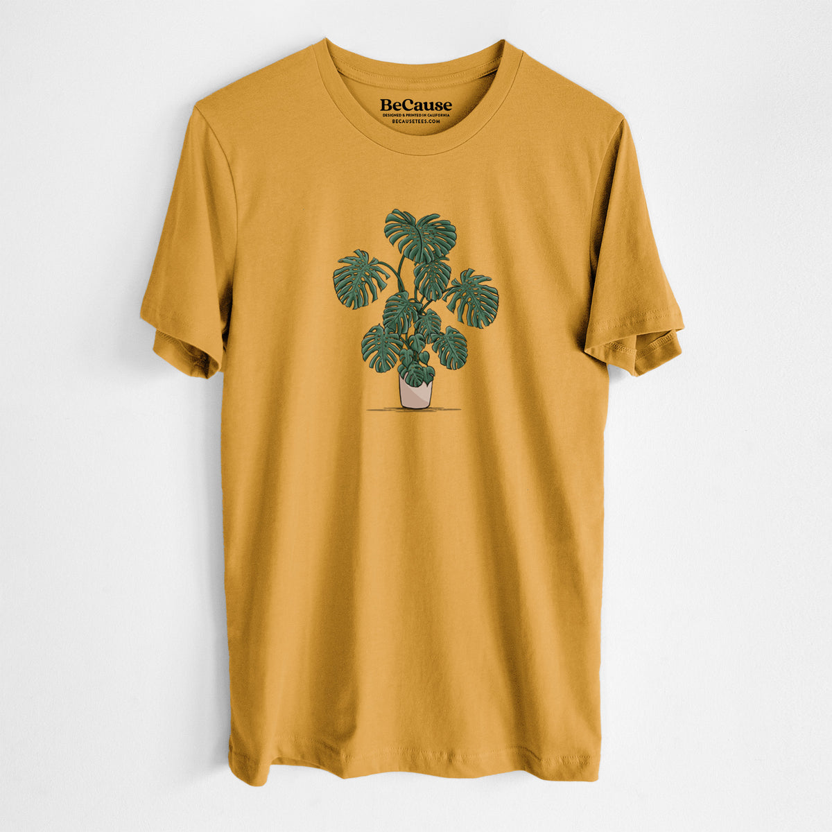 Mustard yellow lightweight cotton t-shirt laid flat, printed with a full-color illustration of a large potted Monstera plant.