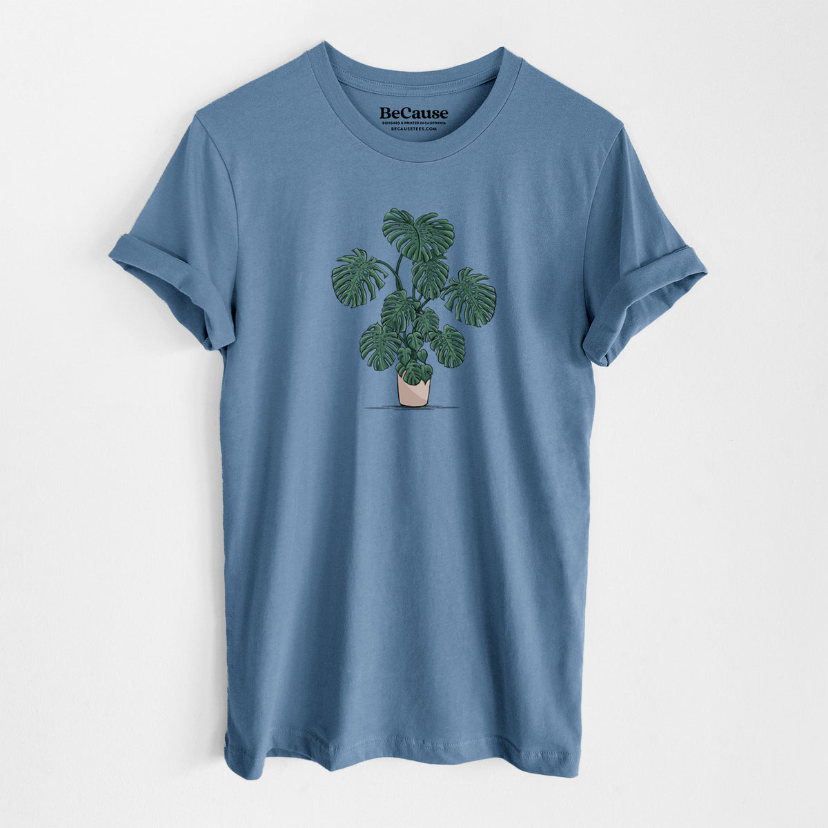 Steel blue lightweight cotton t-shirt laid flat, printed with a full-color illustration of a large potted Monstera plant.
