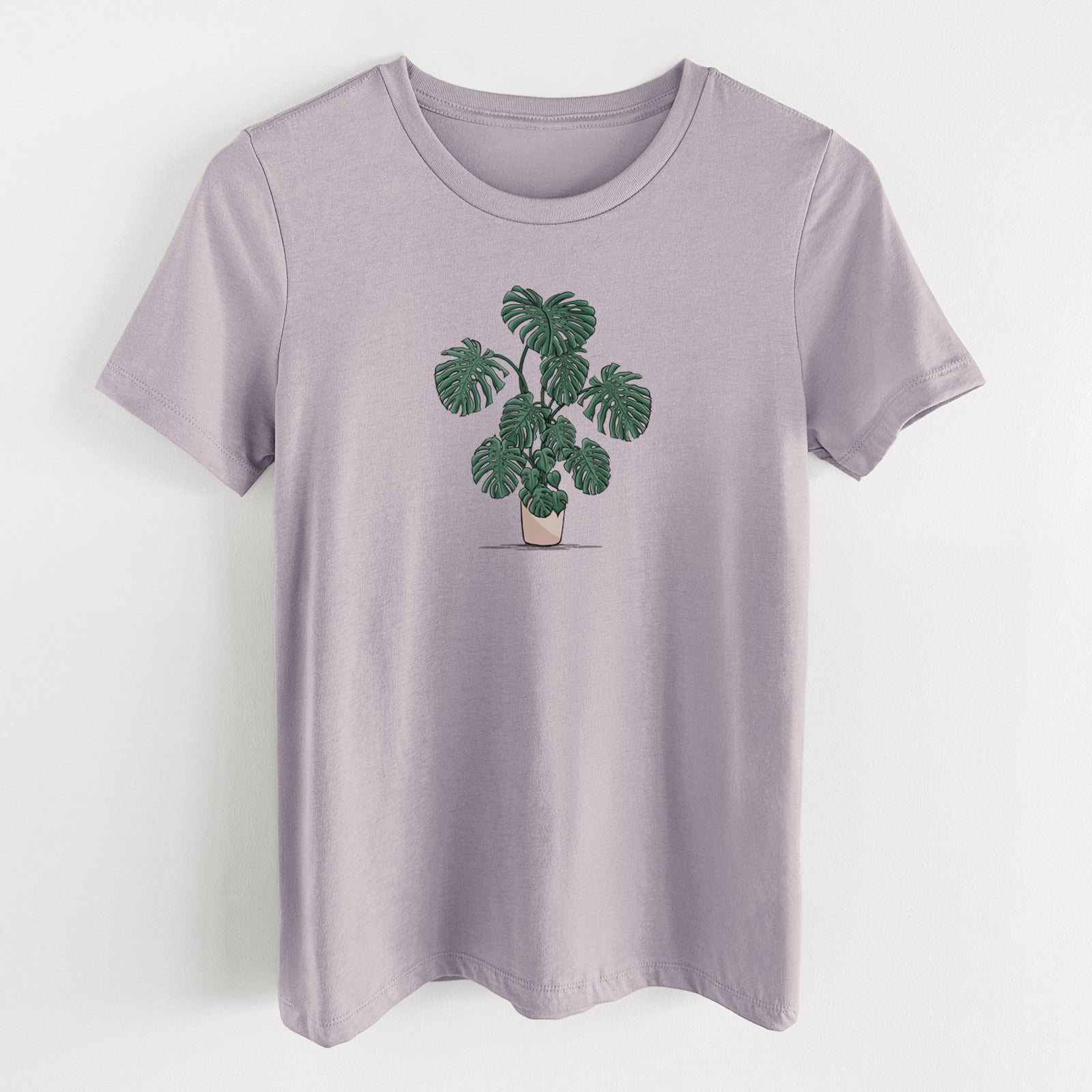 Light violet women's relaxed fit cotton t-shirt laid flat, printed with a full-color illustration of a large potted Monstera plant.