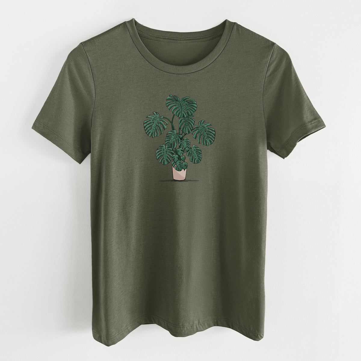 Military green women's relaxed fit cotton t-shirt laid flat, printed with a full-color illustration of a large potted Monstera plant.