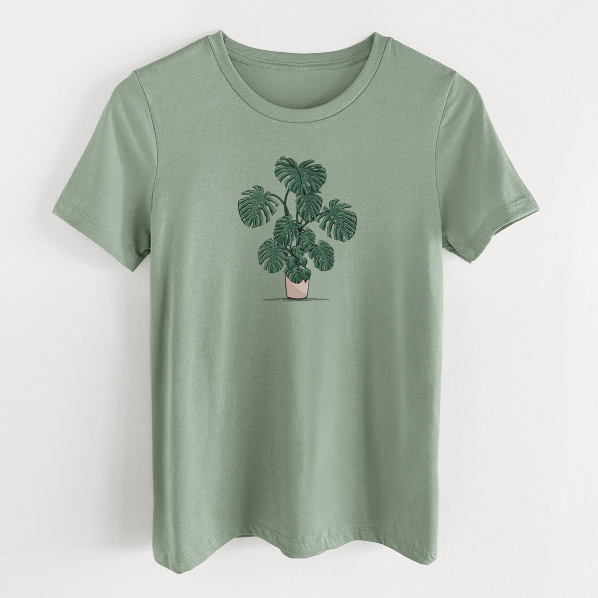 Sage green women's relaxed fit cotton t-shirt laid flat, printed with a full-color illustration of a large potted Monstera plant.