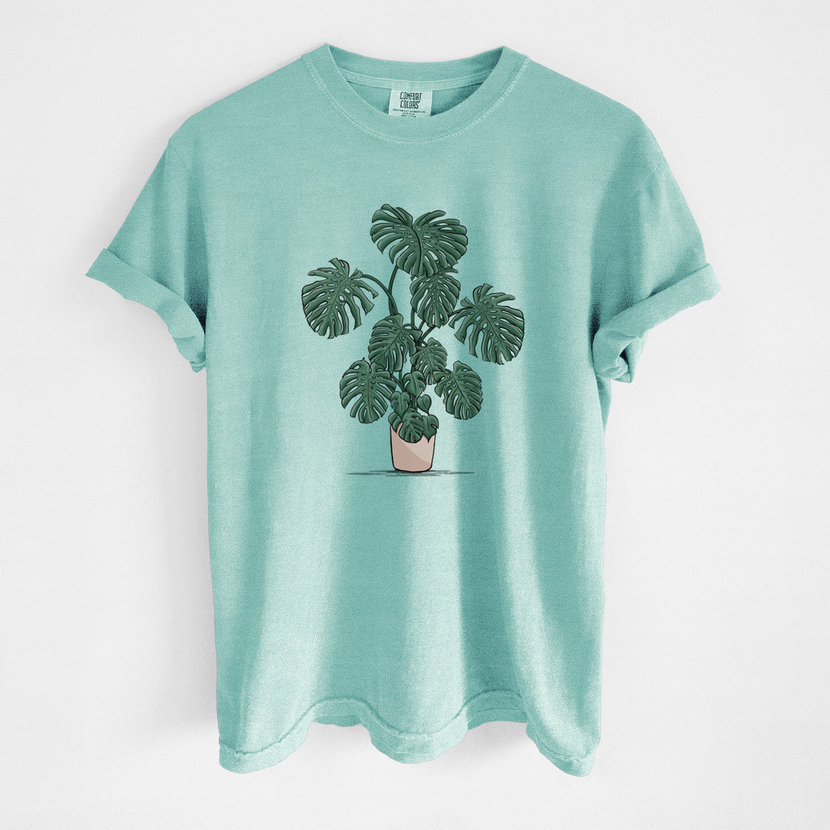 Chalky mint Comfort Colors t-shirt laid flat, printed with a full-color illustration of a large potted Monstera plant.