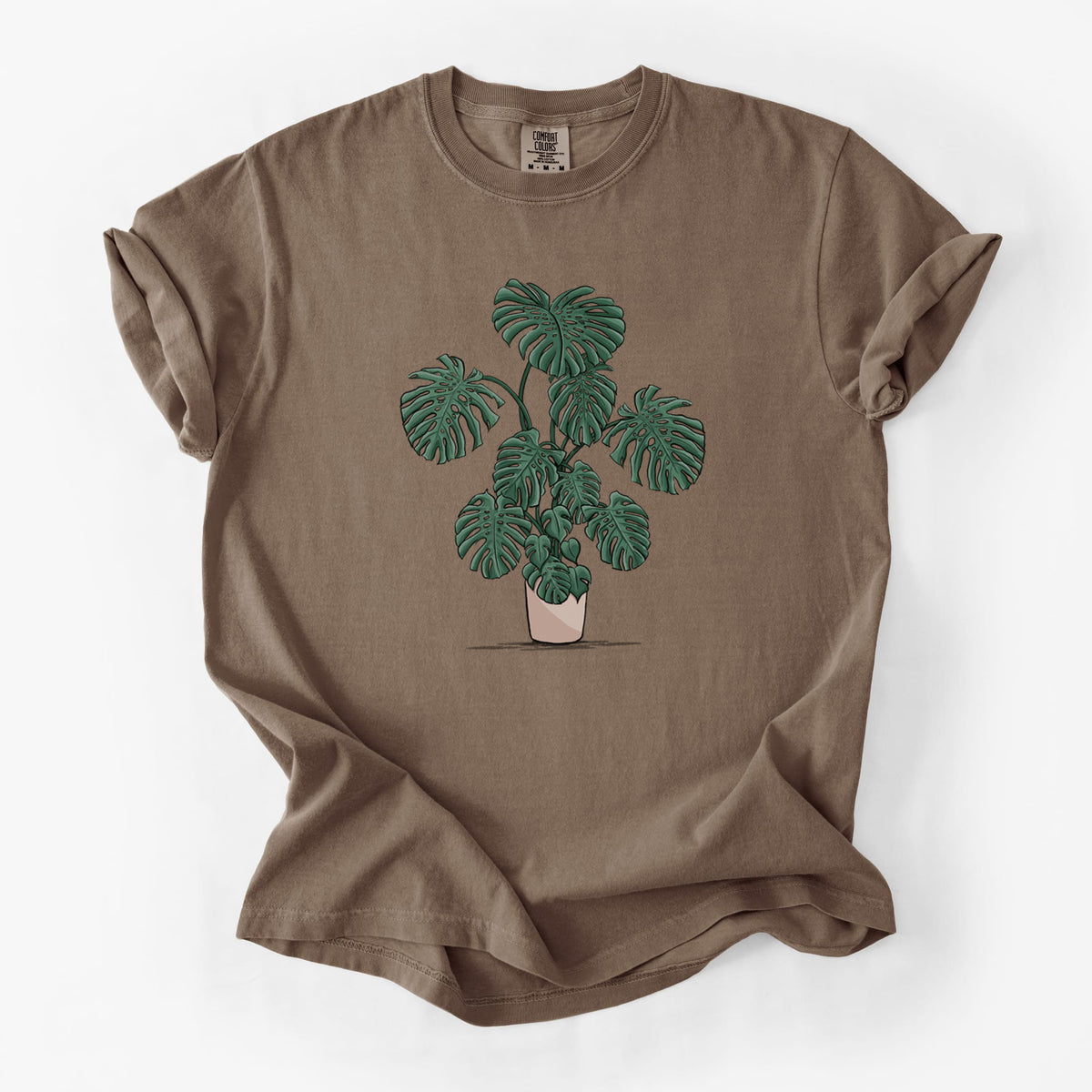 Espresso brown Comfort Colors t-shirt laid flat, printed with a full-color illustration of a large potted Monstera plant.