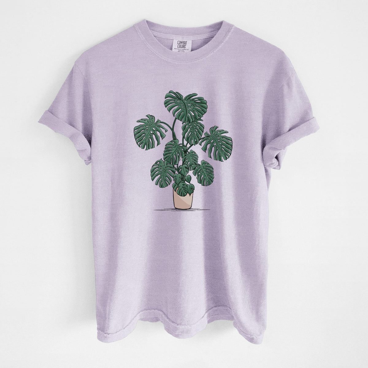 Orchid purple Comfort Colors t-shirt laid flat, printed with a full-color illustration of a large potted Monstera plant.
