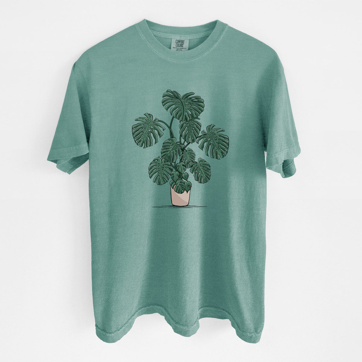 Reef green Comfort Colors t-shirt laid flat, printed with a full-color illustration of a large potted Monstera plant.