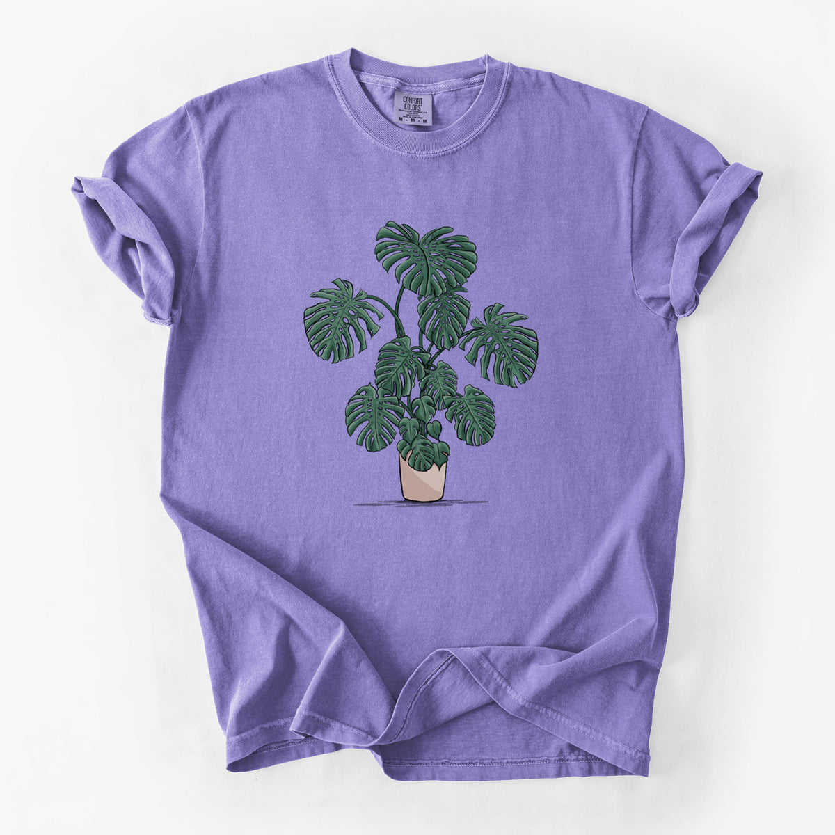 Violet purple Comfort Colors t-shirt laid flat, printed with a full-color illustration of a large potted Monstera plant.