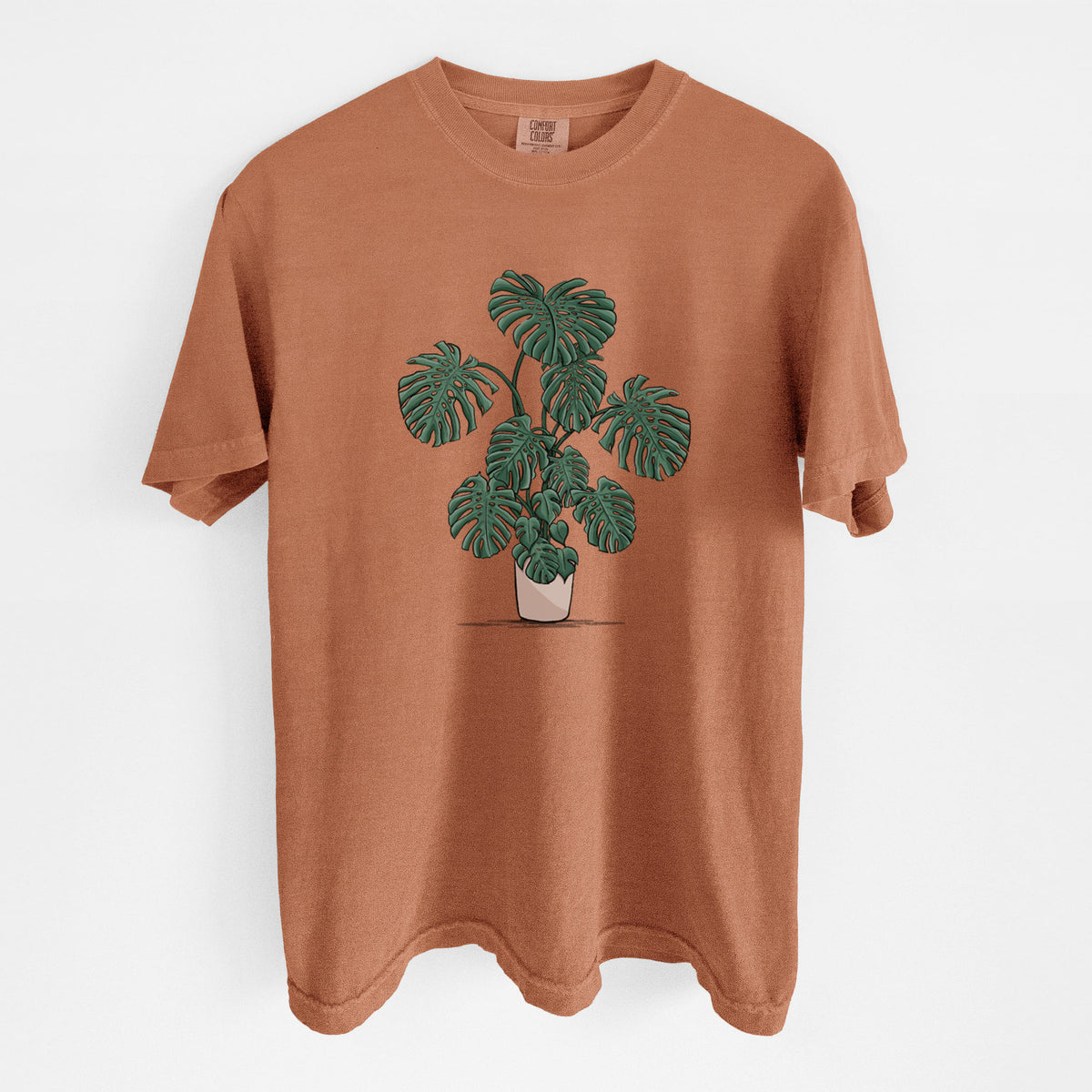 Yam burnt orange Comfort Colors t-shirt laid flat, printed with a full-color illustration of a large potted Monstera plant.