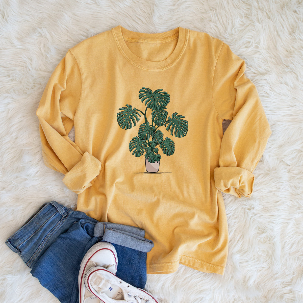 Golden wheat yellow Comfort Colors long sleeve shirt printed with a full-color illustration of a large potted Monstera plant, shown in a lifestyle photo.