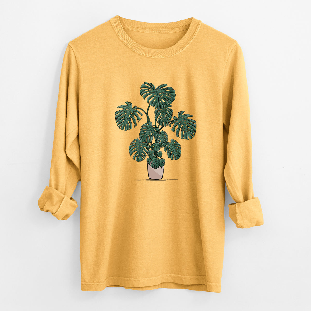 Golden wheat yellow Comfort Colors long sleeve shirt laid flat with the cuffs rolled, printed with a full-color illustration of a large potted Monstera plant.