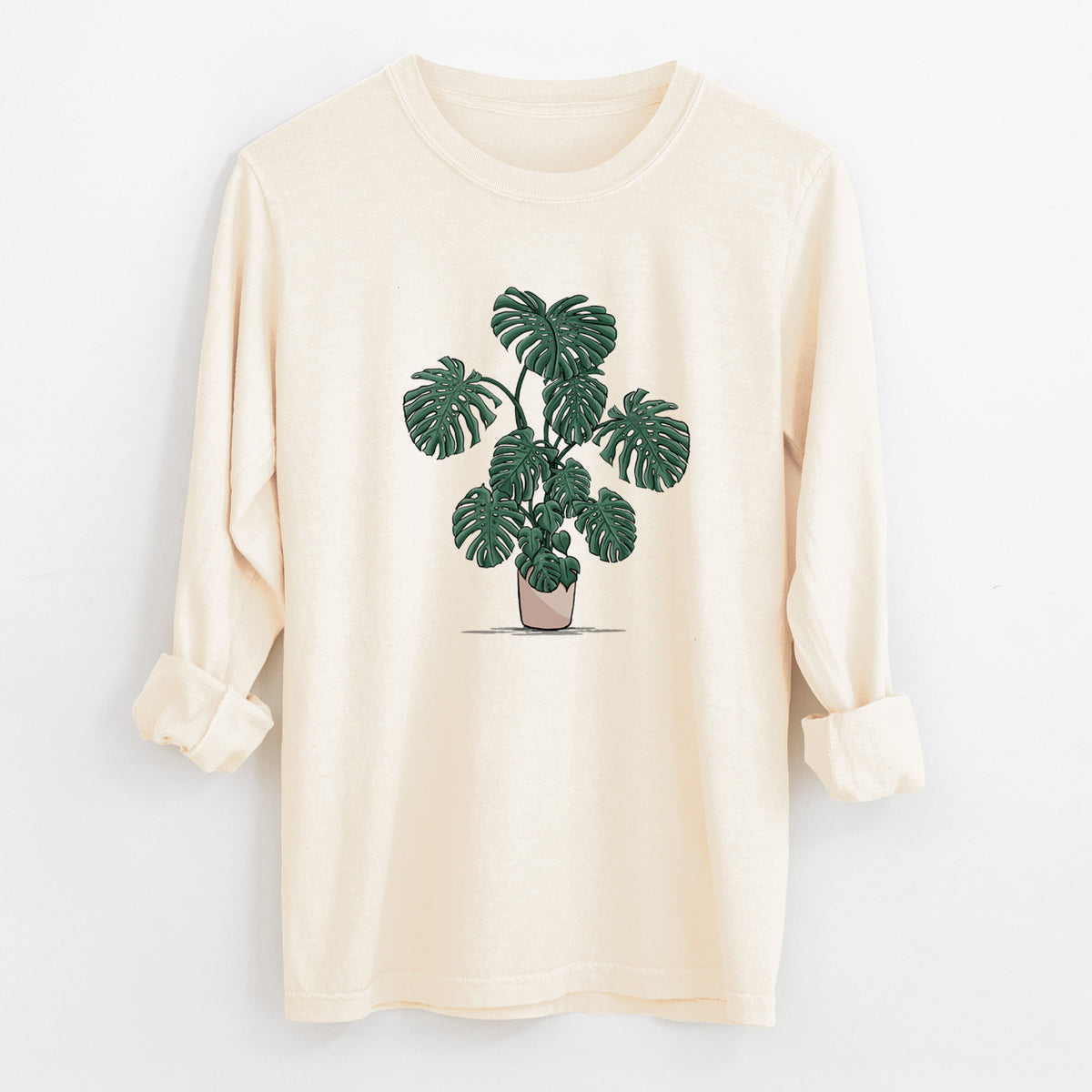 Ivory Comfort Colors long sleeve shirt laid flat with the cuffs rolled, printed with a full-color illustration of a large potted Monstera plant.