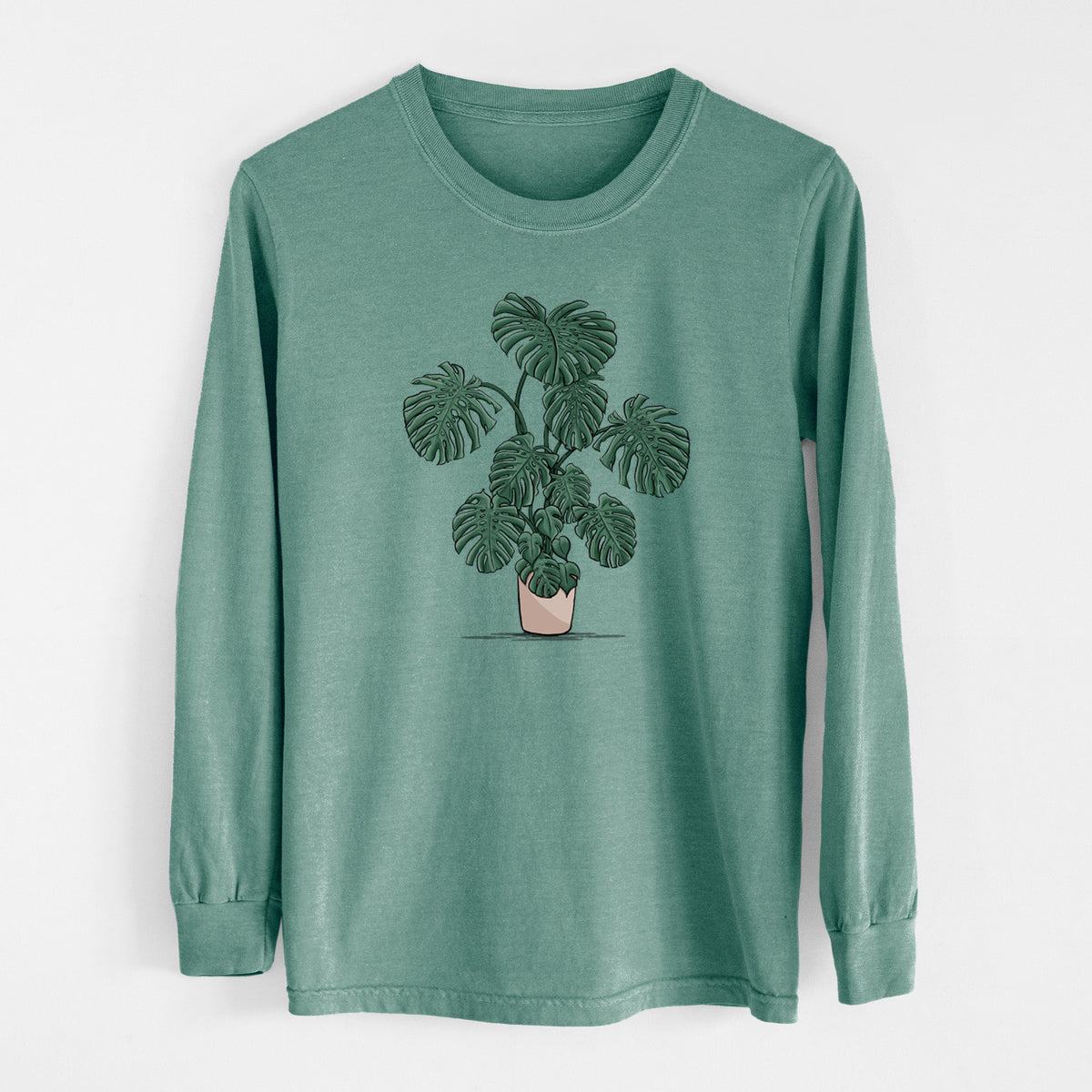 Pine green Comfort Colors long sleeve shirt laid flat, printed with a full-color illustration of a large potted Monstera plant.