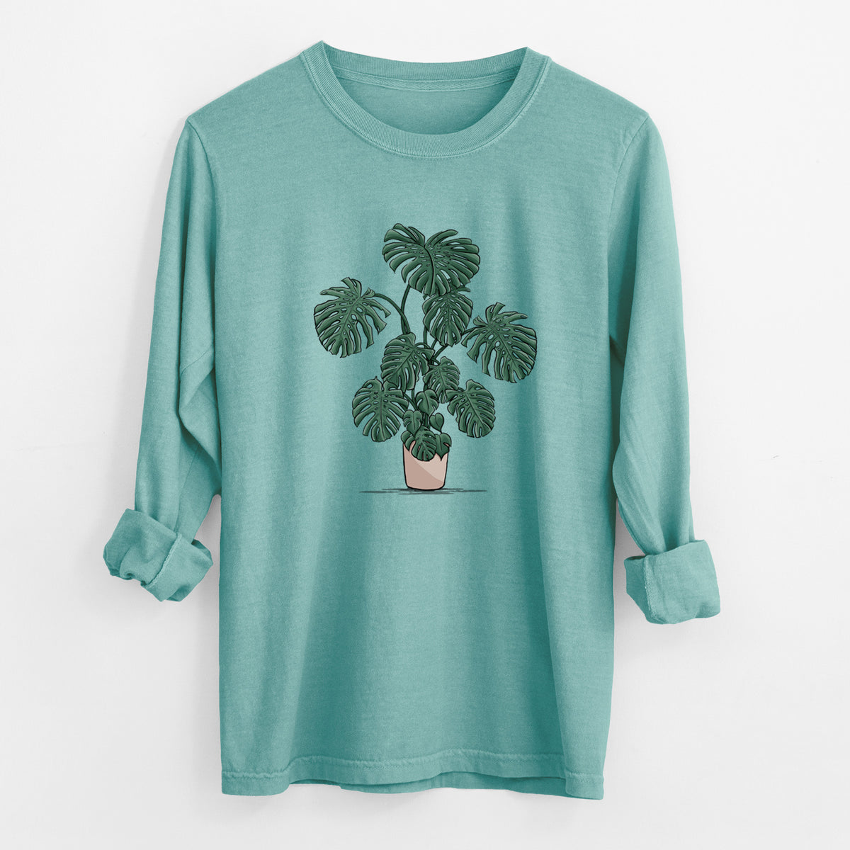 Reef green Comfort Colors long sleeve shirt laid flat with the cuffs rolled, printed with a full-color illustration of a large potted Monstera plant.